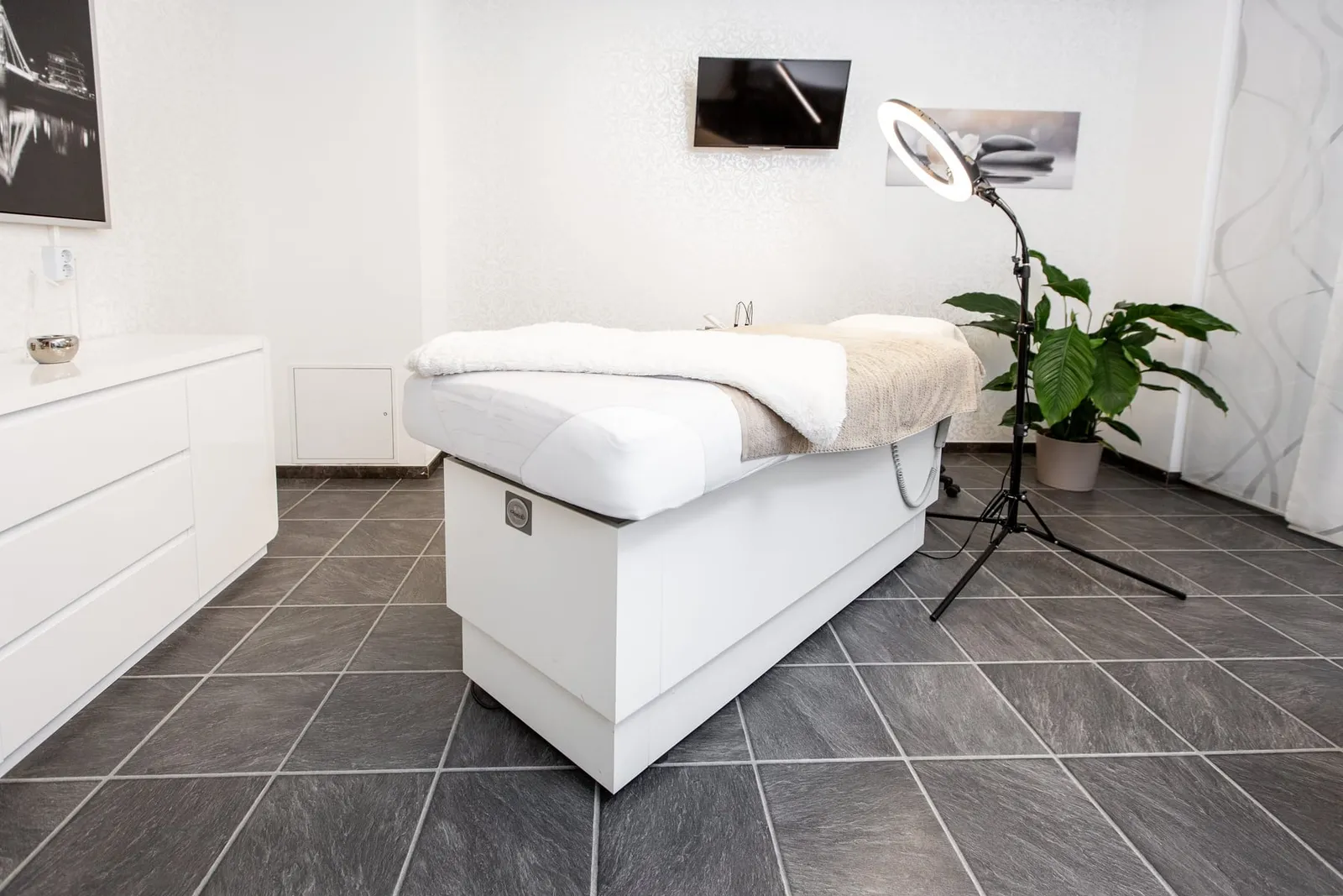 Behandlungsliege mit Handtuch, Ringleuchte und Pflanze.