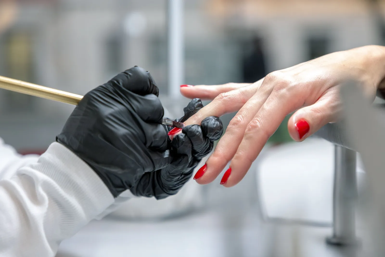 Hand mit schwarzem Handschuh lackiert einen Fingernagel rot.
