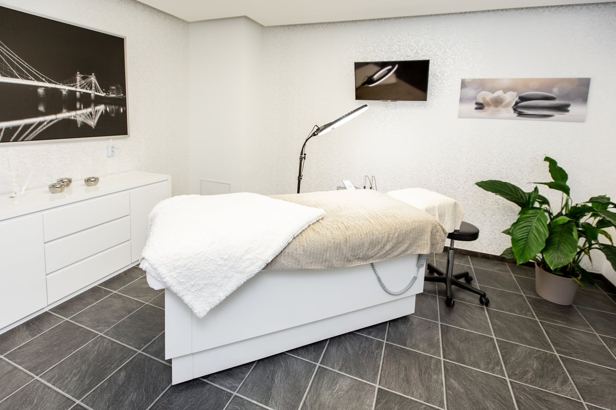 Heller Behandlungsraum im Studio mit Liege, Lampe und Pflanze.